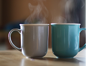 Two hot coffee mugs on a table; condensed vapor is shown rising from the coffee into the air.
