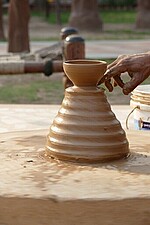 A pottery wheel with a clay pot and a hand touching it
