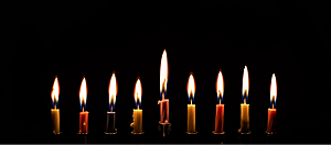 Photo of several candle flames with long wicks pulling melted was up from below.