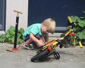 A picture of a young child pumping up his bike tires with a stand pump.