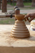 A pottery wheel with a clay pot and a hand touching it